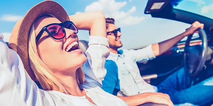 Zwei Personen sitzen in einem Cabrio und fahren auf einer Straße bei sonnigem Wetter