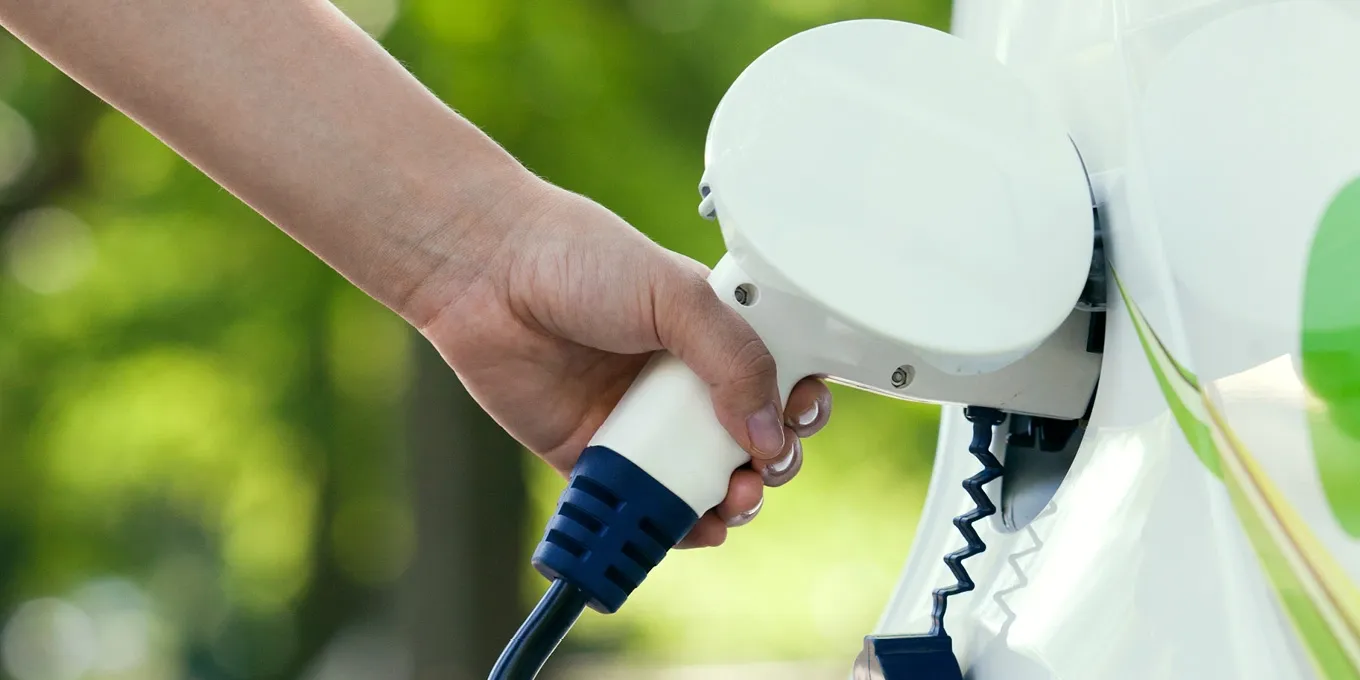 Person lädt ein Elektroauto mit einem Ladestecker