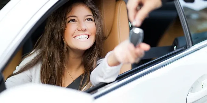 Person sitzt am Steuer eines Fahrzeugs und erhält einen Autoschlüssel durch das geöffnete Seitenfenster