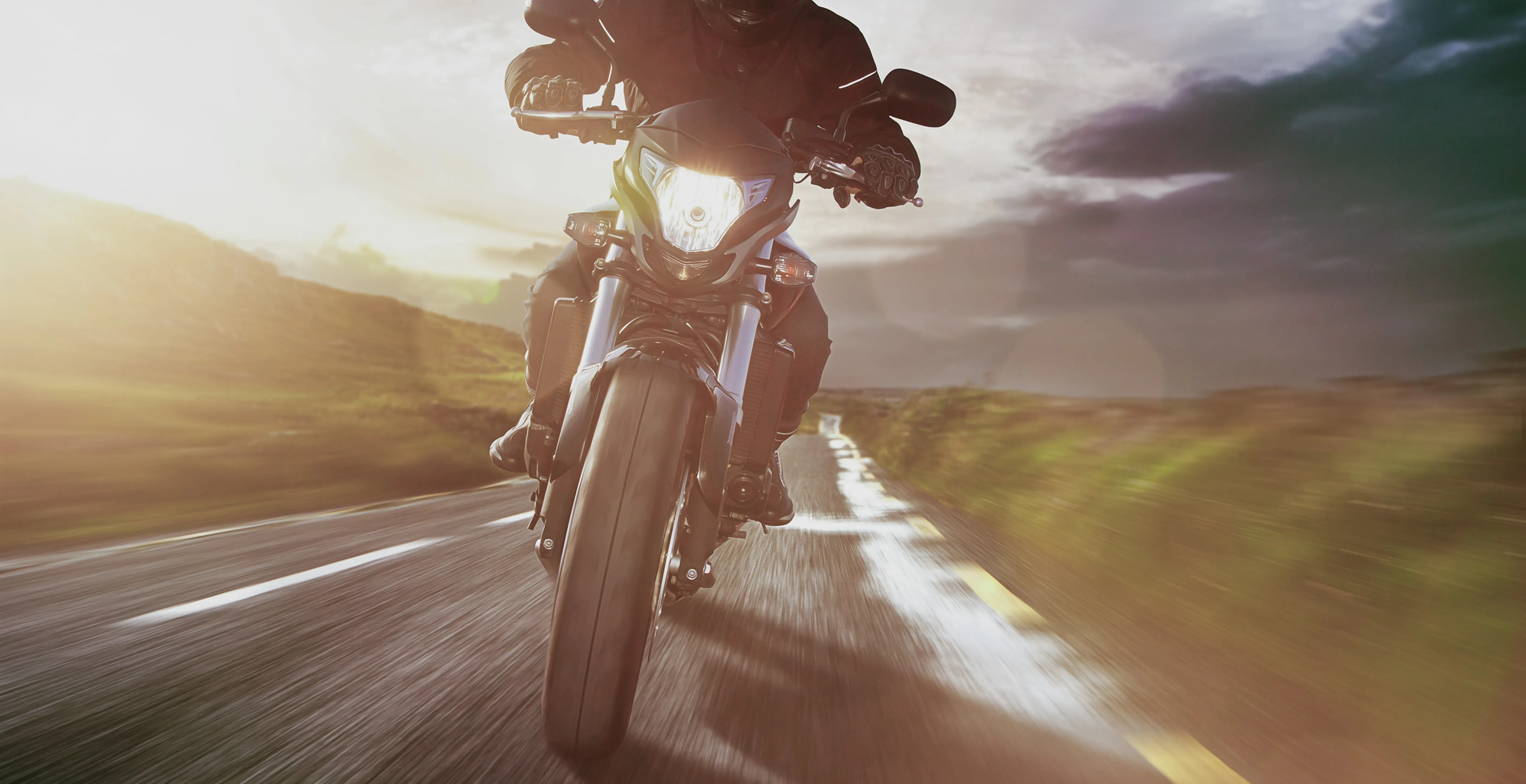 Person fährt Motorrad auf einer Landstraße bei tiefstehender Sonne