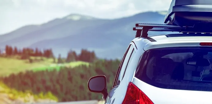 Auto auf Reise mit Dachbox vor Berglandschaft und Naturkulisse