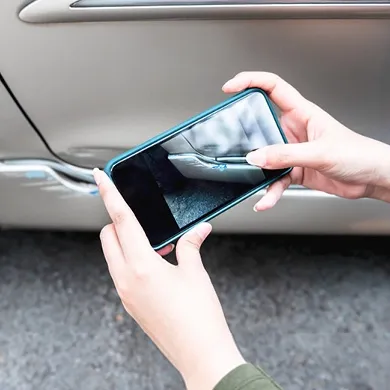 Person fotografiert einen Schaden an einem Auto mit dem Smartphone